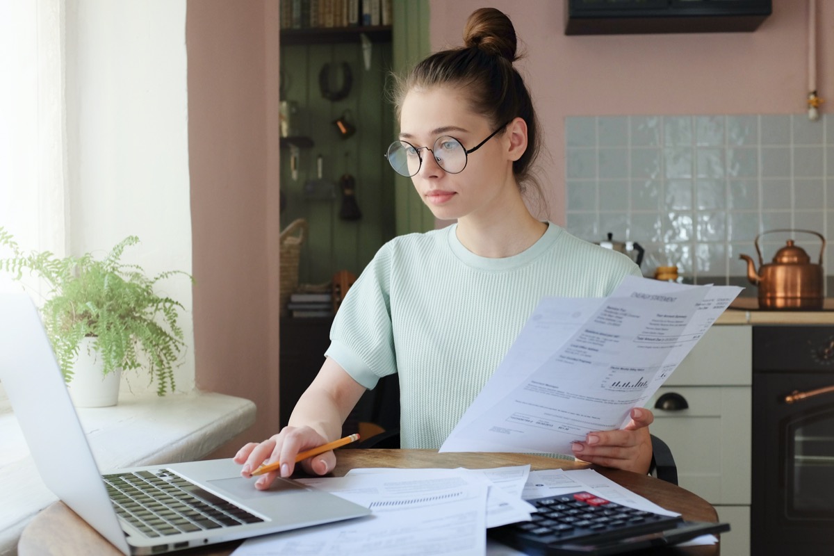 young white woman sitting at laptop holding bills