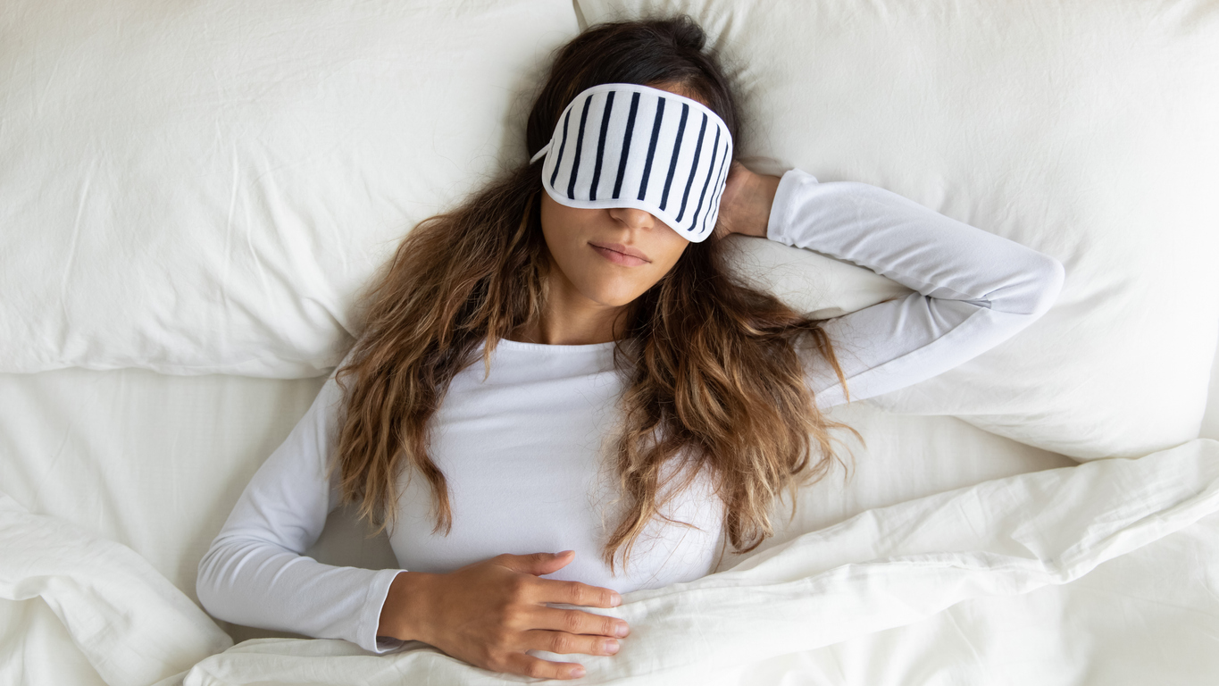 A young woman wearing an eye mask sleeping peacefully in bed.