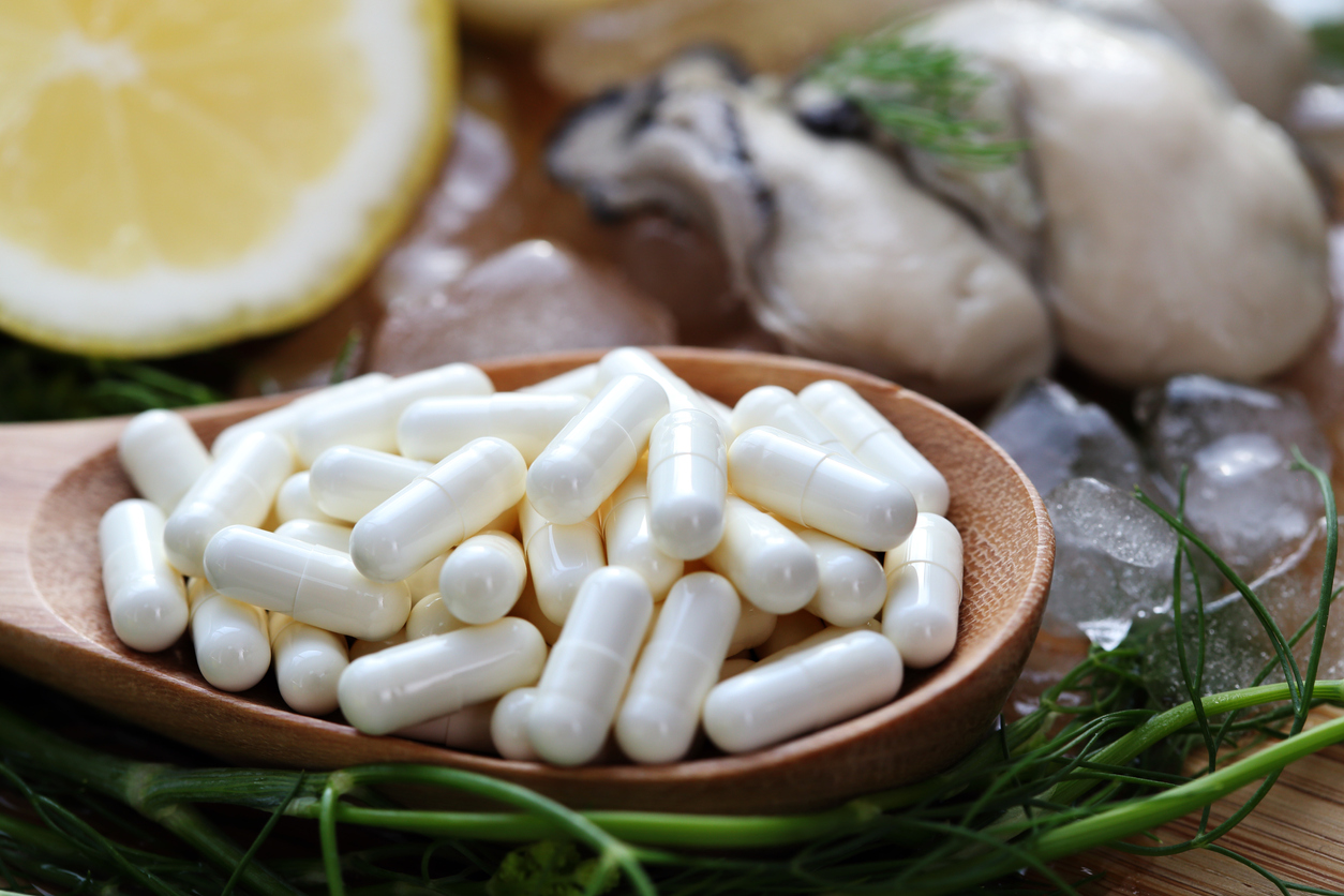 Zinc supplement capsules sit in a bowl in front of a fresh oyster and sliced lemon.