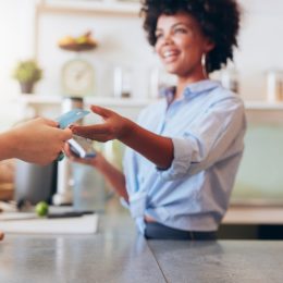 Cropped shot of female employee taking payment from customer, focus on female hands giving credit card for juice bar payment.