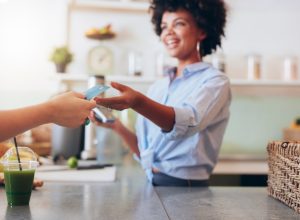 Cropped shot of female employee taking payment from customer, focus on female hands giving credit card for juice bar payment.