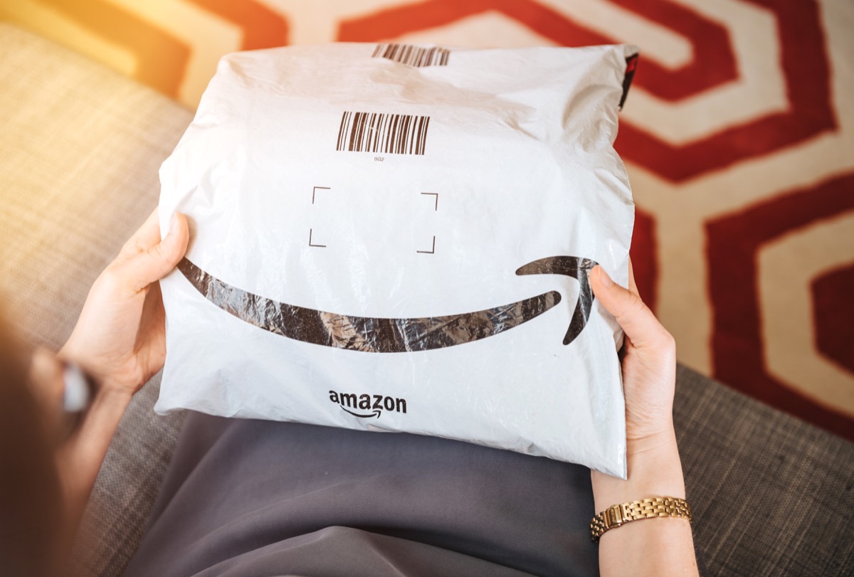 Overhead view of elegant woman on living room couch holding fresh Amazon Prime plastic package parcel with iconic logotype smile