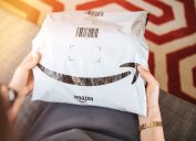 Overhead view of elegant woman on living room couch holding fresh Amazon Prime plastic package parcel with iconic logotype smile
