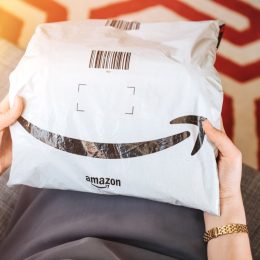 Overhead view of elegant woman on living room couch holding fresh Amazon Prime plastic package parcel with iconic logotype smile