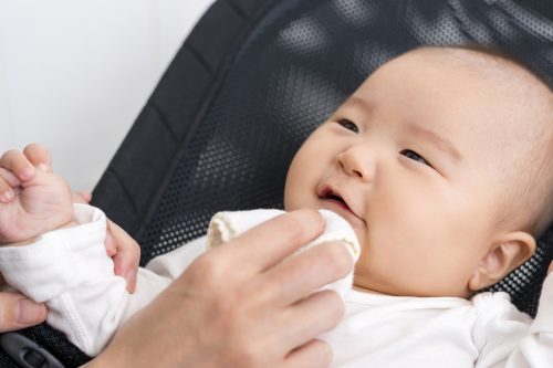 Nahaufnahme der Hand, die das Gesicht des asiatischen Babys in der Wippe abwischt