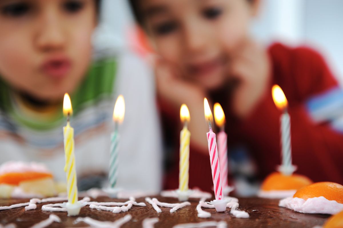 Two little boys blowing candles on cake at birthday party