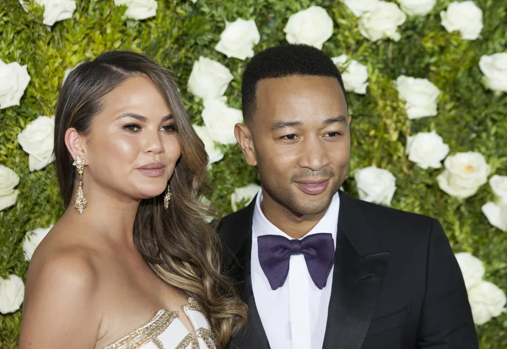 Chrissy Teigen and John Legend standing in front of a green wall