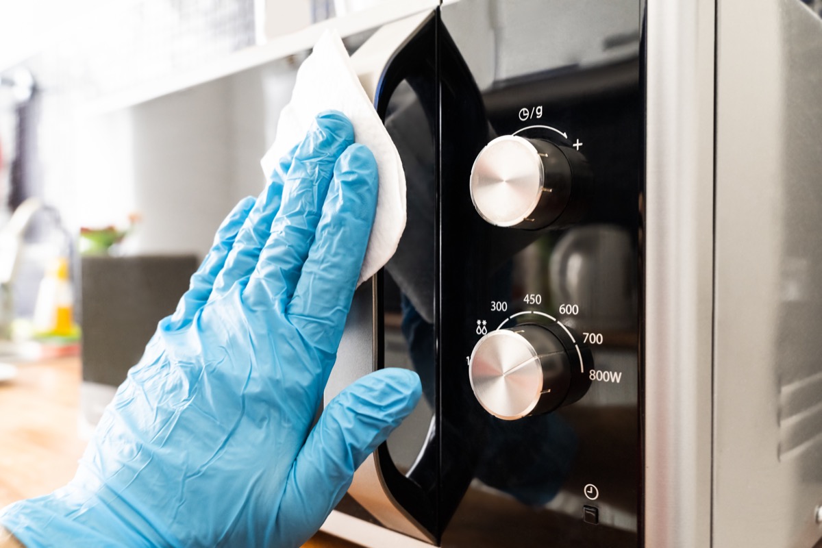 Man Wiping Microwave Oven Handle With Sanitizer Against Virus Infection