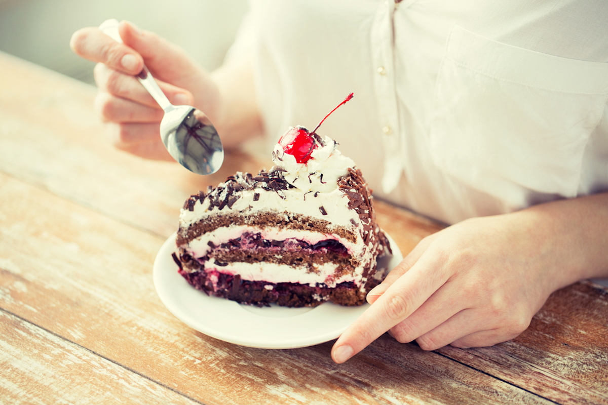 close up of woman eating chocolate cherry cake with spoon and sitting at wooden table