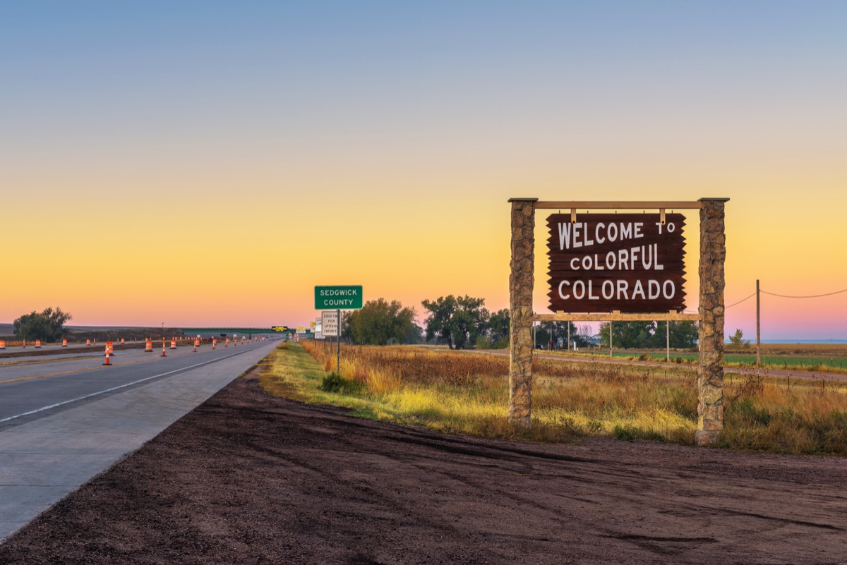a wooden "Welcome to Colorful Colorado" sign off of the highway at sunset