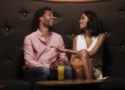 Cheerful young couple laughing while conversing on sofa at nightclub