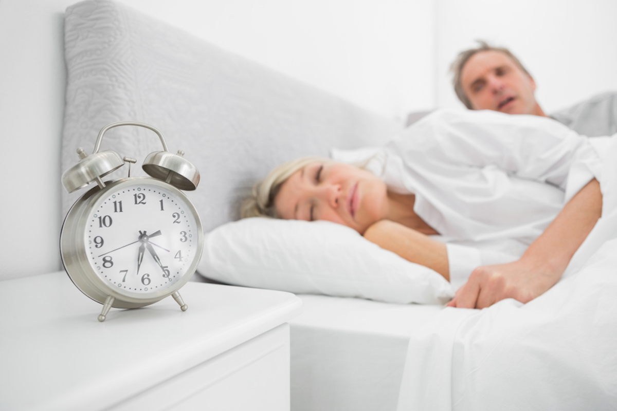 woman sleeps through alarm while husband looks annoyed