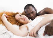 white woman with red hair and black man look frustrated while laying down together