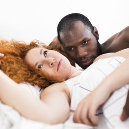 white woman with red hair and black man look frustrated while laying down together