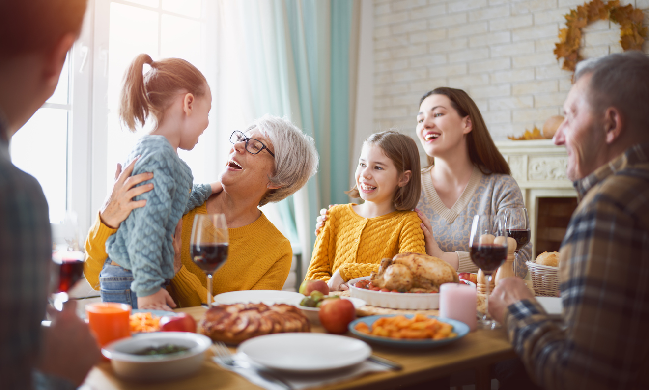 A family celebrates Thanksgiving at the dinner table while a mother and daughter watch on as a grandmother hugs her grandaughter