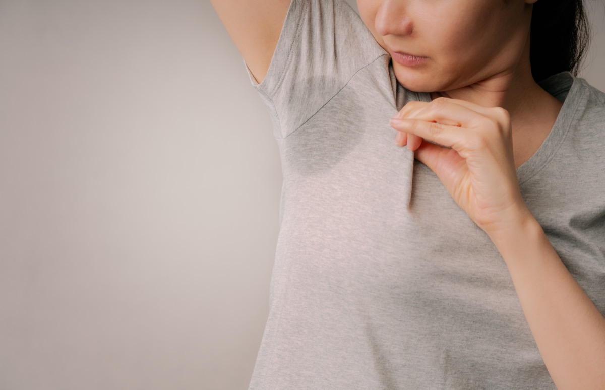 Femeie atrăgătoare stânjenită de petele de transpirație de pe cămașa ei gri.  Femeile asiatice miros urât de transpirație pe subsuoară cu fundal gri.  Concepte de îngrijire a sănătății și hiperhidroză sau transpirație excesivă