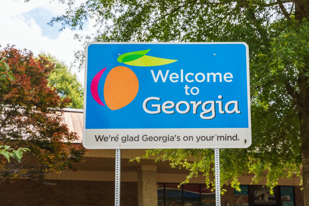 a blue "Welcome to Georgia" sign in front of trees and a building