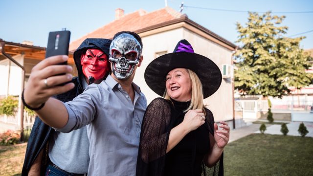 Young man with a skeleton mask taking selfie with his friends in Halloween