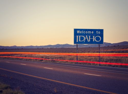 a blue "Welcome to Idaho" sign off of a highway at dusk