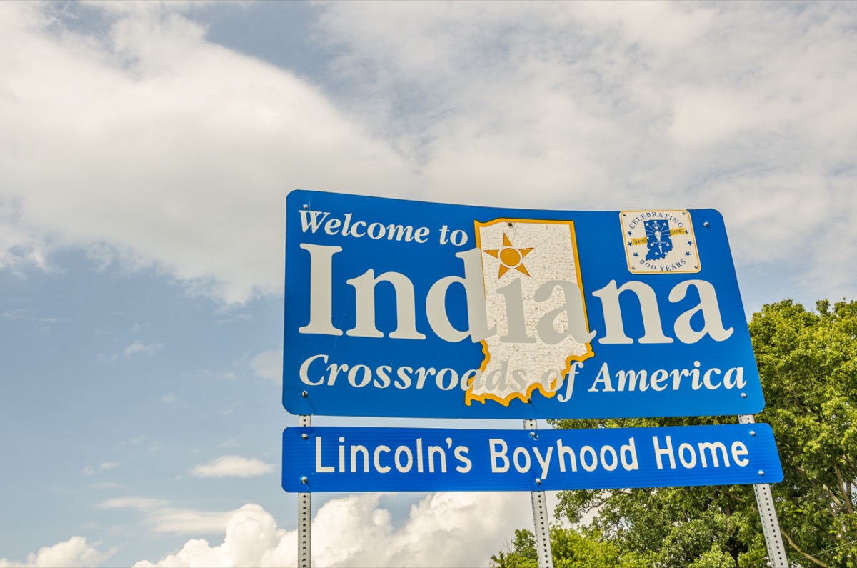 a blue "Welcome to Indiana" sign in front of green trees