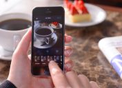 İstanbul, Turkey - January 23, 2015: Woman hands holding an Apple iPhone 5s and taking photos of a dessert and coffee cup with Instagram application. iPhone is a touchscreen smart phone produced by Apple Inc.