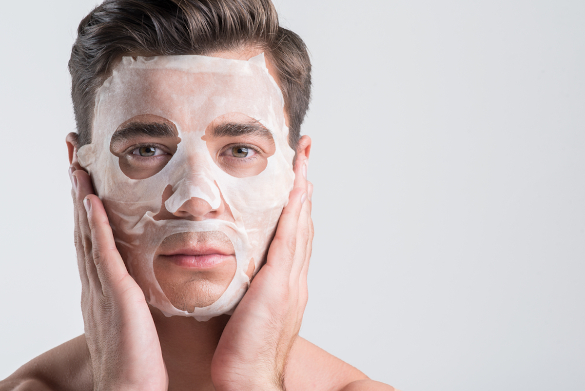 man wearing sheet mask with brown hair and brown eyes on grey background