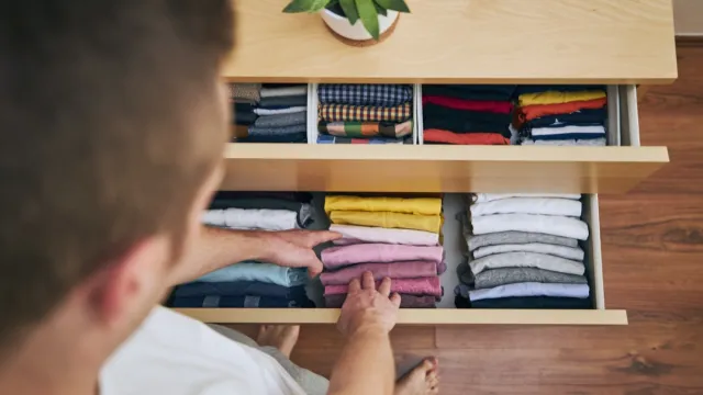 Organizing and cleaning home. Man preparing orderly folded t-shirts in drawer.
