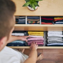 Organizing and cleaning home. Man preparing orderly folded t-shirts in drawer.