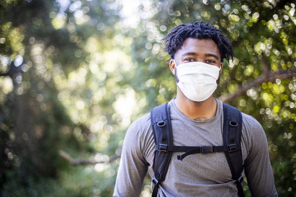 A young black man wearing a face mask on a hike