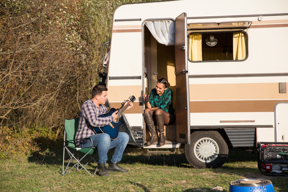 young white straight couple playing guitar outside camper van