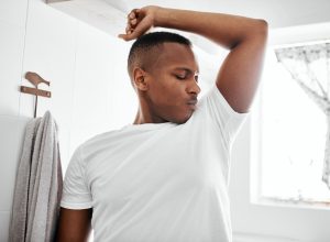 Shot of a young man smelling his underarms while standing in the bathroom