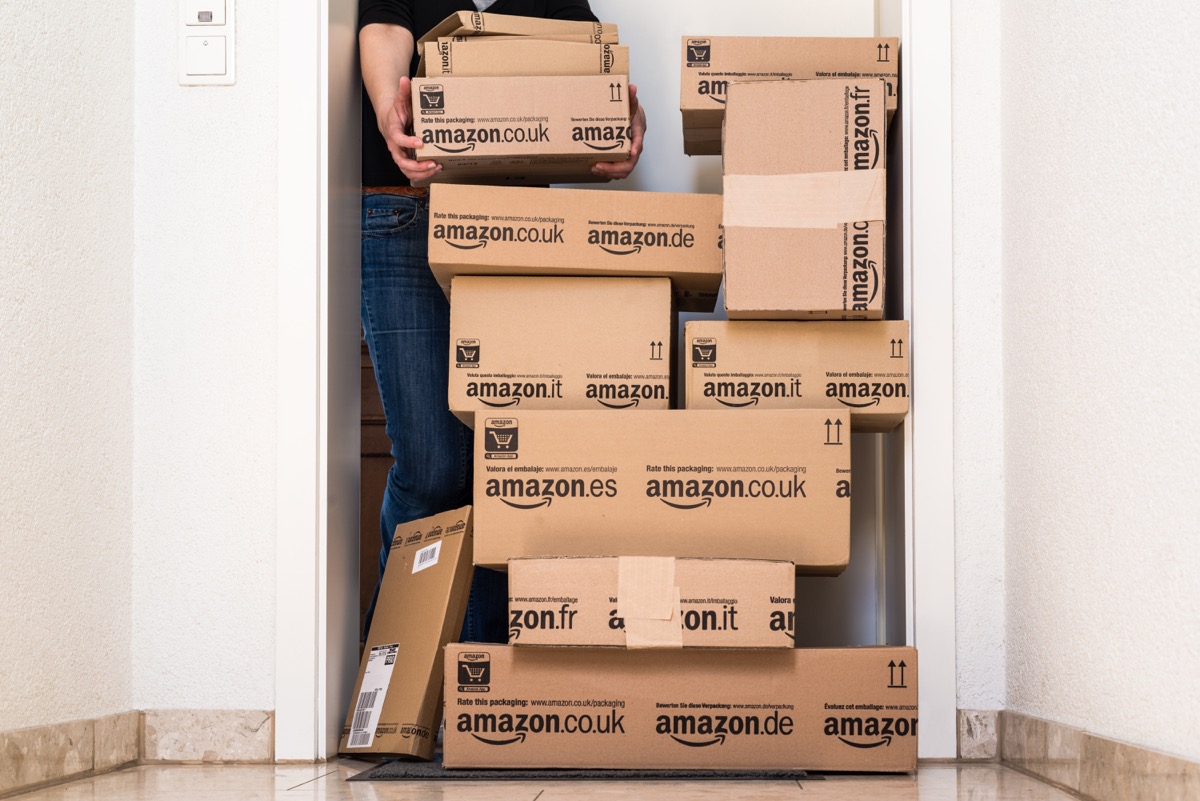 Ostfildern, Germany - May 18, 2014: A woman is horrified by a large stack of parcels by Amazon.com in different sizes waiting in front of the entrance door to her flat on May, 18, 2014 in Ostfildern-Scharnhausen near Stuttgart, Germany. This conceptual photo can serve different purposes: It might demonstrate the domination of Amazon.com in the area of online shopping or the trend in general to shop online for all the different items you need in your personal life.