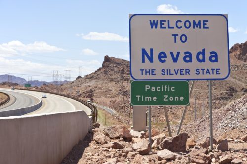 a white "Welcome to Nevada" sign off of a highway and within dirt and rocks