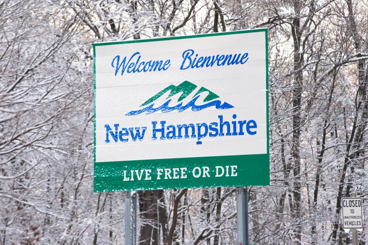 a white "New Hampshire" sign in front of trees that have snow on them