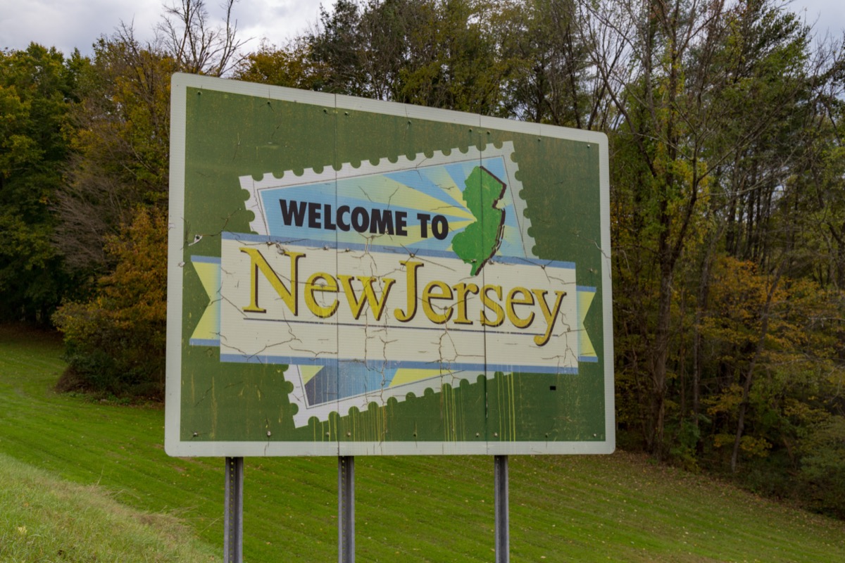 a green "Welcome to New Jersey" sign in front of green and yellow trees