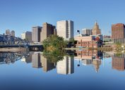 The skyline of Newark, New Jersey as shot from the Passaic River with a rail bridge on the left of the frame