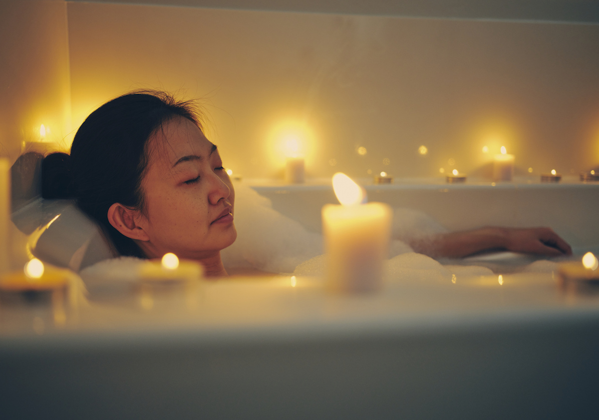 A young Asian woman relaxing in a bathtub, surrounded by candle
