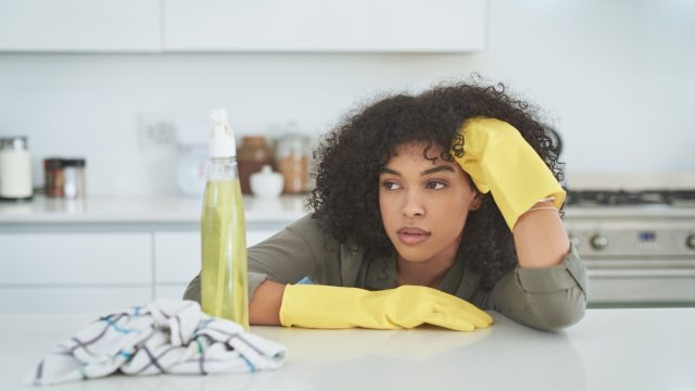 Shot of a young woman looking tired while cleaning a kitchen counter at home