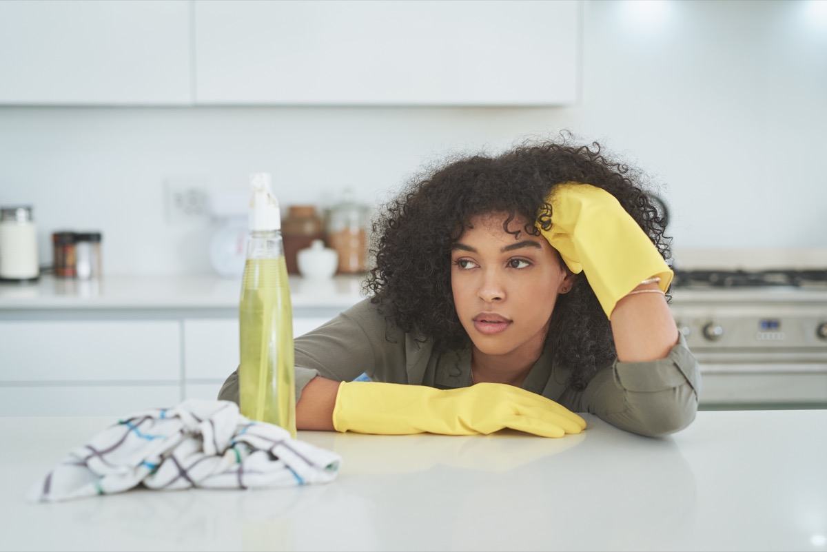 Shot of a young woman looking tired while cleaning a kitchen counter at home