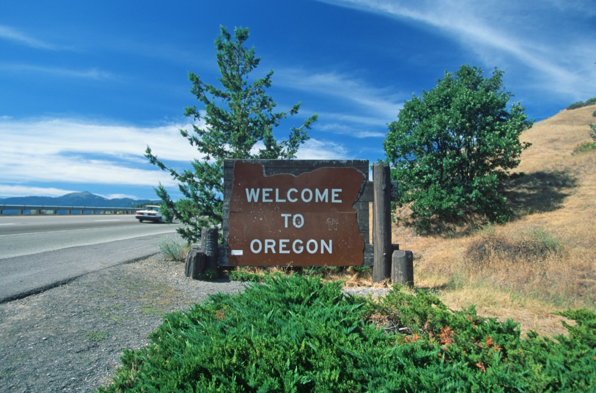 a wooden "Welcome to Oregon" sign in front of trees and off of a highway