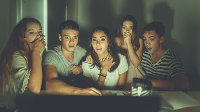 College students watching scary movie on laptop