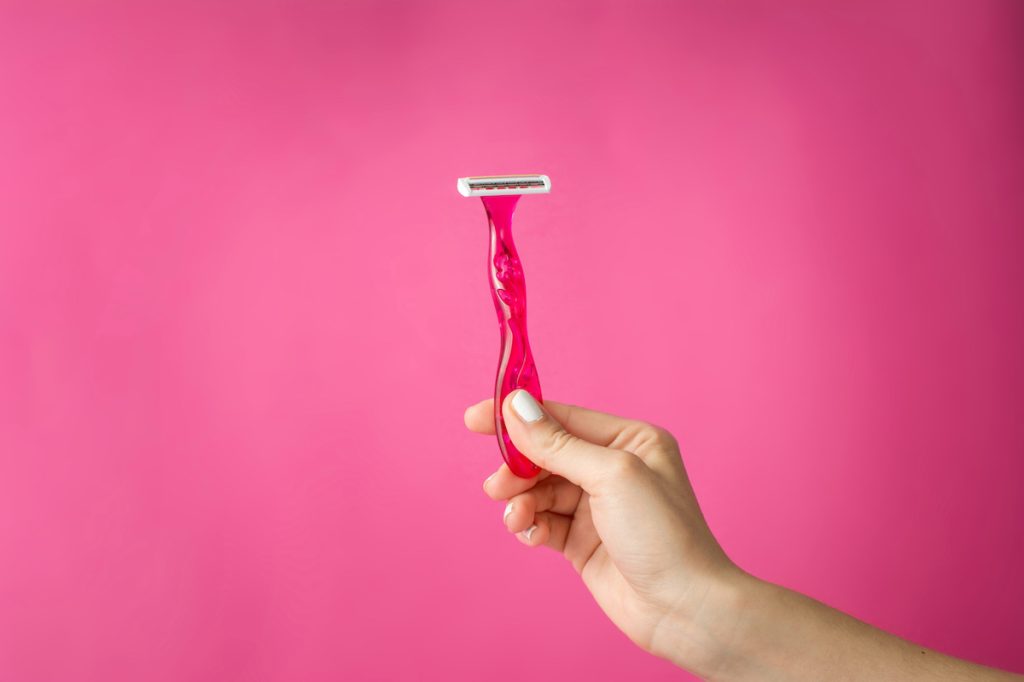 Red shaver in woman's hands against pink background