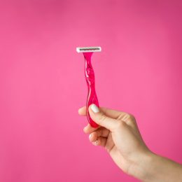 Red shaver in woman hands against pink background