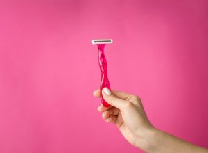Red shaver in woman hands against pink background