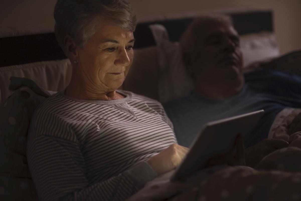 woman browsing the Internet late at the night while husband sleeps