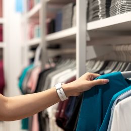 Close up of woman hand shopping or choosing casual blue color t-shirt on rack at department store