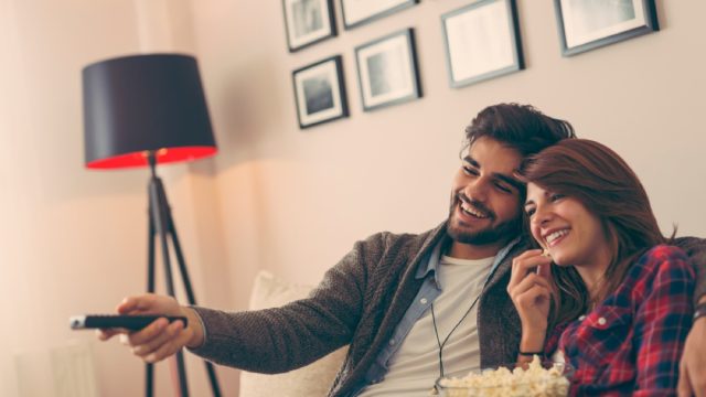 young man and woman watching tv and eating popcorn on the couch