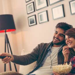 young man and woman watching tv and eating popcorn on the couch