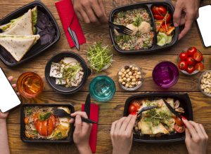 An above shot of takeout food in containers on a table as people eat.