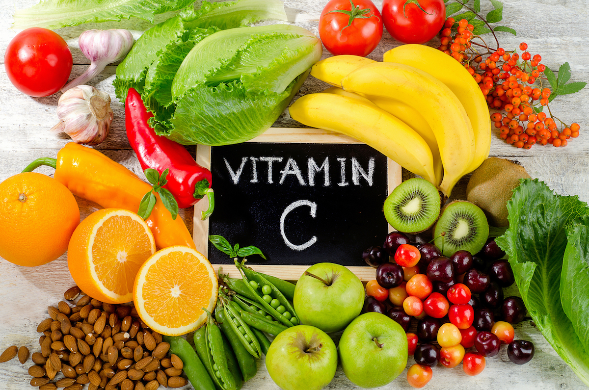Foods High in vitamin C on a wooden board, including oranges, almonds, kiwis, bananas, peppers, and more